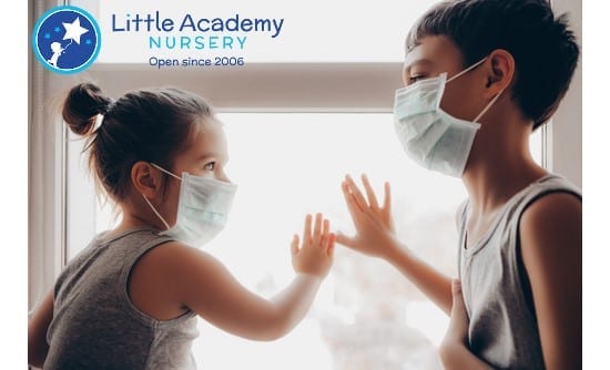 A girl wearing a mask on her face is holding right hand of the boy who is also wearing a mask is standing in front of him.